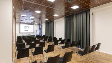 Sala conferenze con sedie nere disposte di fronte a uno schermo e tavolo frontale