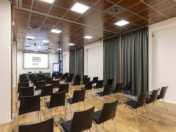 Sala conferenze con sedie nere disposte di fronte a uno schermo e tavolo frontale