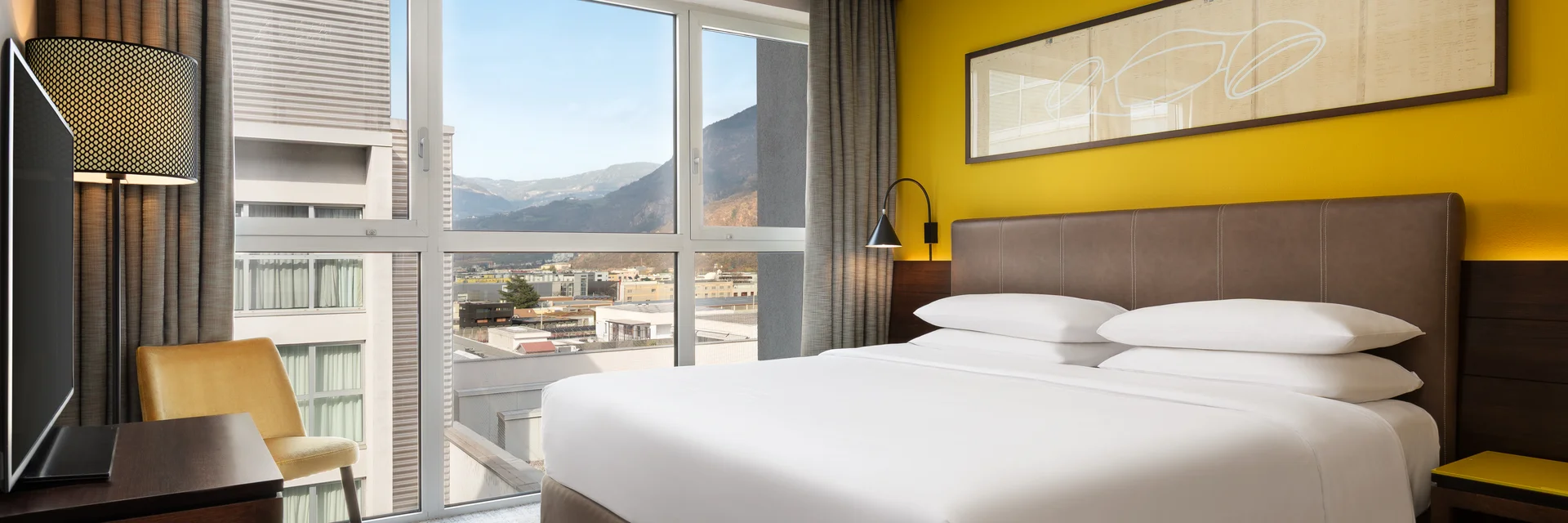 Camera d'hotel moderna con letto matrimoniale, scrivania e vista sulle montagne