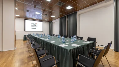 Sala riunioni con tavolo a U, bottiglie d'acqua e proiettore Four Points Bolzano