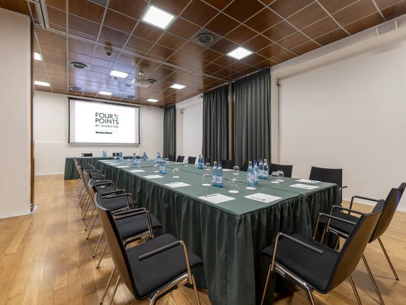 Sala riunioni con tavolo a U, bottiglie d'acqua e proiettore Four Points Bolzano