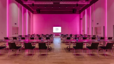Sala conferenze con illuminazione rosa e sedie disposte attorno a tavoli