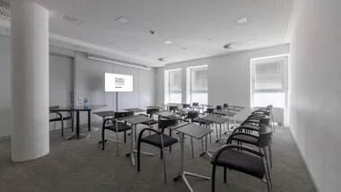 Sala conferenze con sedie e tavolini davanti a uno schermo in un ambiente moderno