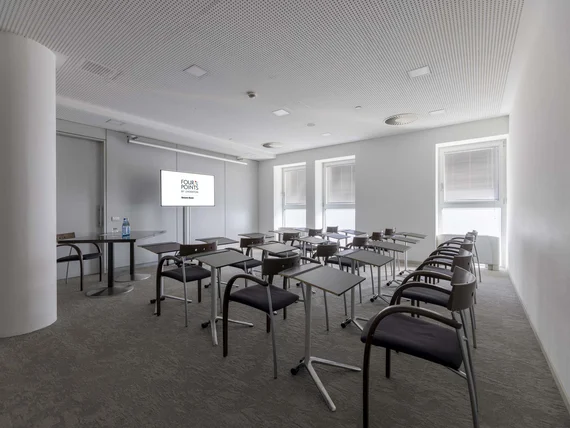 Sala conferenze con sedie e tavolini davanti a uno schermo in un ambiente moderno