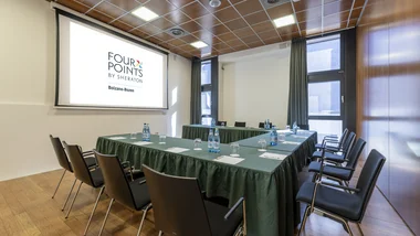 Sala riunioni con tavoli a U, sedie nere e schermo proiettore Four Points Bolzano