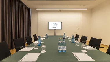 Sala riunioni con tavolo verde e monitor con logo Four Points by Sheraton