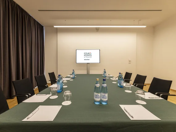 Sala riunioni con tavolo verde e monitor con logo Four Points by Sheraton