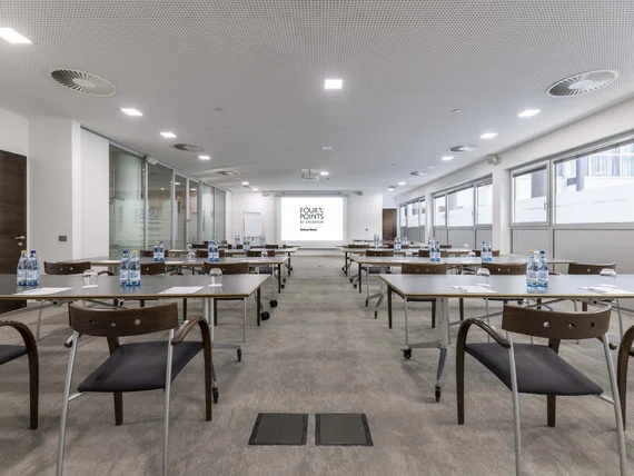 Sala conferenze con tavoli, sedie, acqua e proiettore Four Points