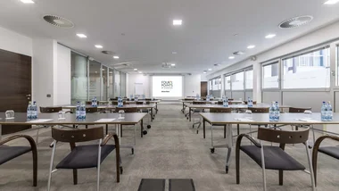 Sala conferenze con tavoli, sedie, acqua e proiettore Four Points