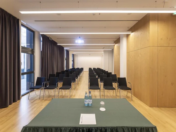 Sala conferenze con file di sedie nere e tavolo frontale con bottiglie d'acqua