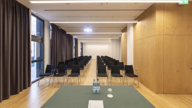 Sala conferenze con file di sedie nere e tavolo frontale con bottiglie d'acqua