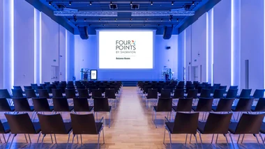 Sala conferenze con sedie e schermo con logo Four Points by Sheraton Bolzano.