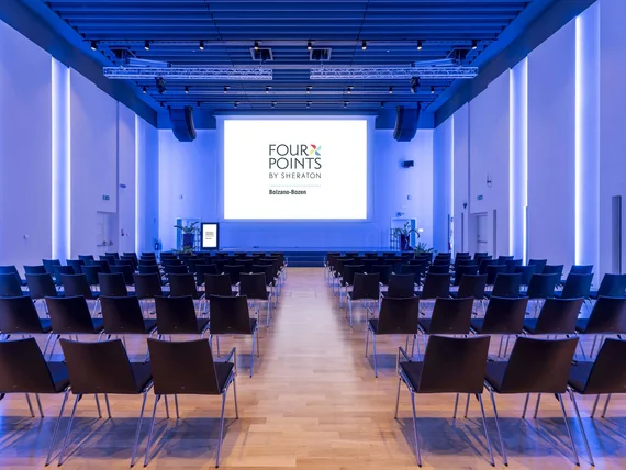 Sala conferenze con sedie e schermo con logo Four Points by Sheraton Bolzano.